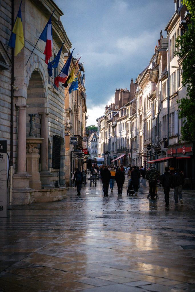 Passants sous la pluie devant des drapeaux, illustrant la protection sociale et mutuelle santé au quotidien.