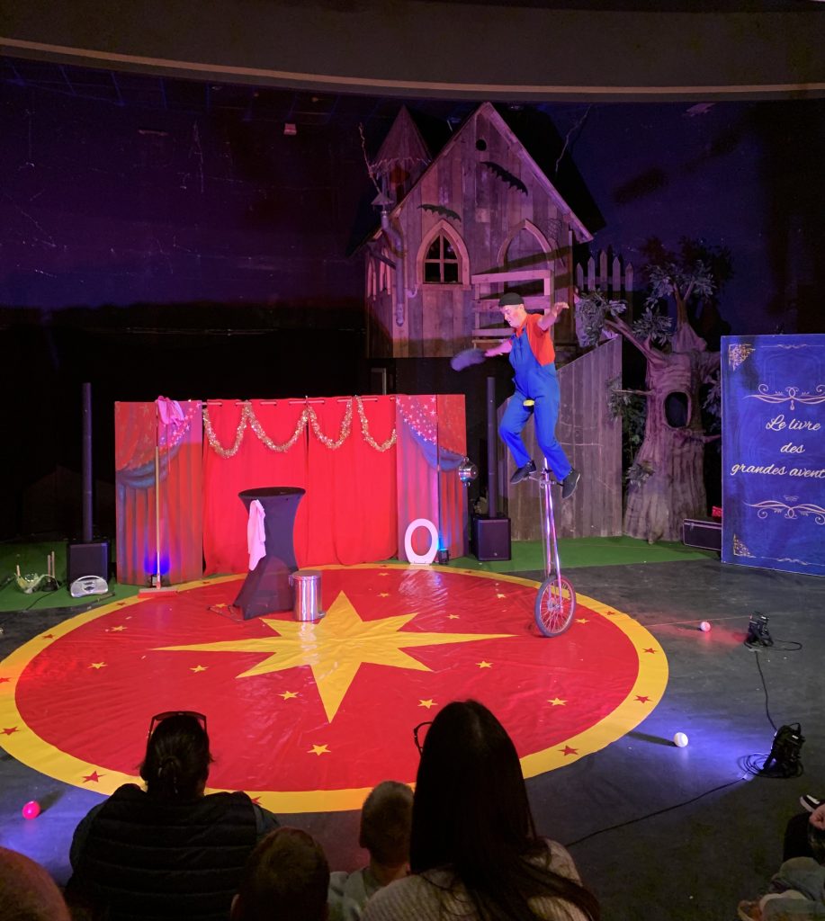Artiste en costume bleu et rouge sur monocycle, promotion mutuelle santé sur scène de cirque.