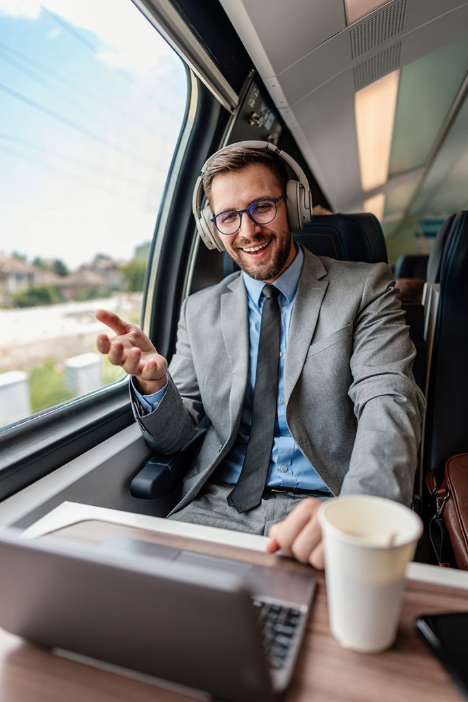 Homme en visio dans le train, discutant mutuelle santé avec café et ordinateur, sourire assuré.