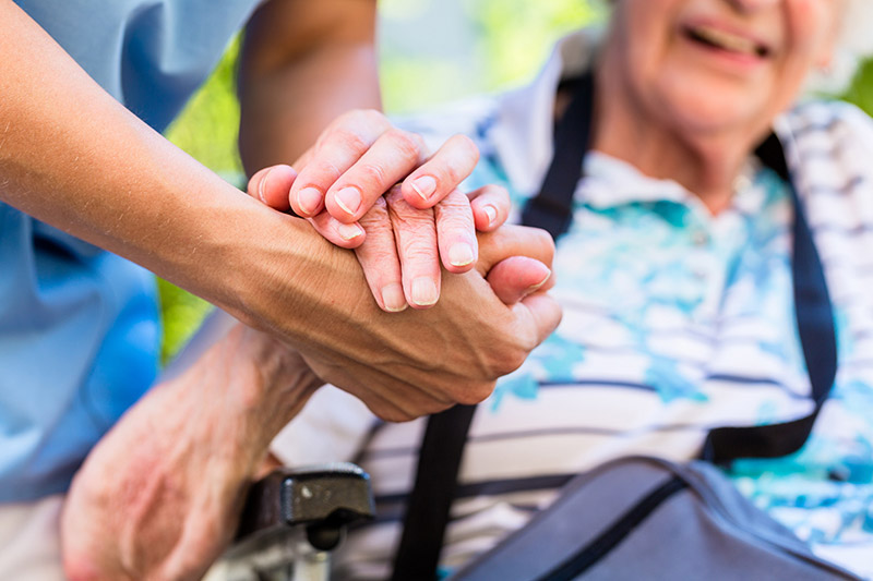Aide-soignant tenant la main d'un sénior en fauteuil, illustrant mutuelle santé et protection sociale.