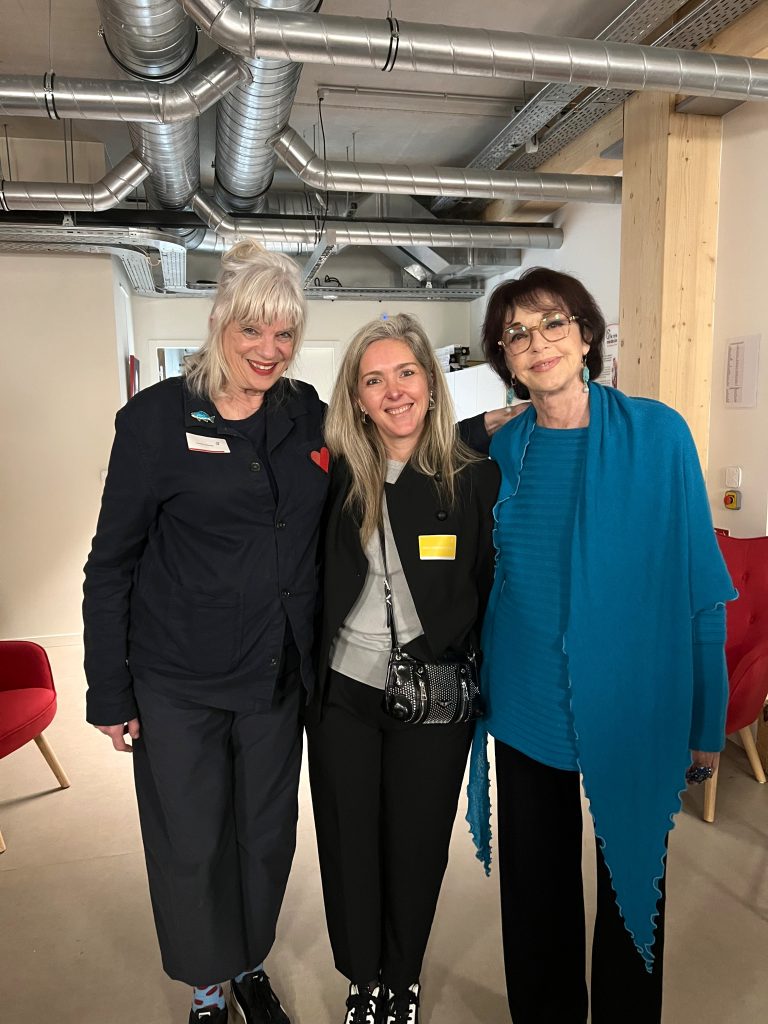 Trois femmes souriantes discutent de mutuelle santé dans un espace moderne au décor industriel.