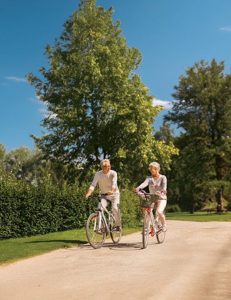 Deux seniors font du vélo au parc, symbole de mutuelle santé et protection sociale efficace.