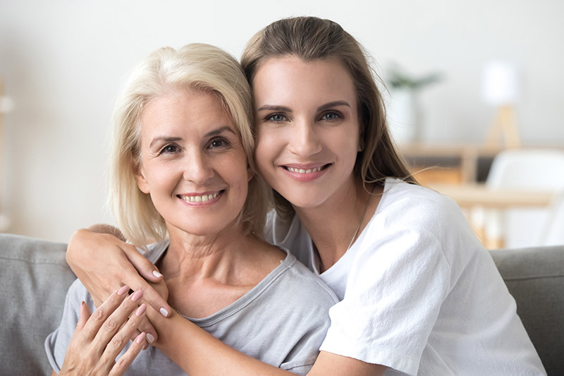 Deux femmes souriantes sur un canapé, évoquant la mutuelle santé et la protection sociale en famille.