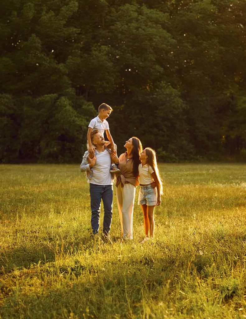 Famille heureuse dans un champ ensoleillé, illustrant la sérénité d'une bonne santé complémentaire.