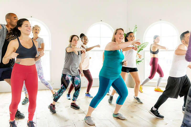Groupe en séance fitness, souriant sous arches lumineuses, illustrant mutuelle santé et protection sociale.
