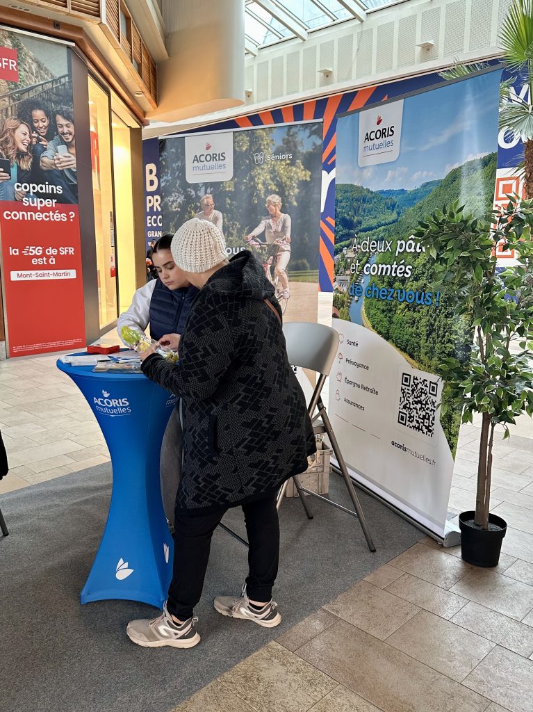 Échange avec le public sur un stand Acoris Mutuelles, devant des supports de communication.
