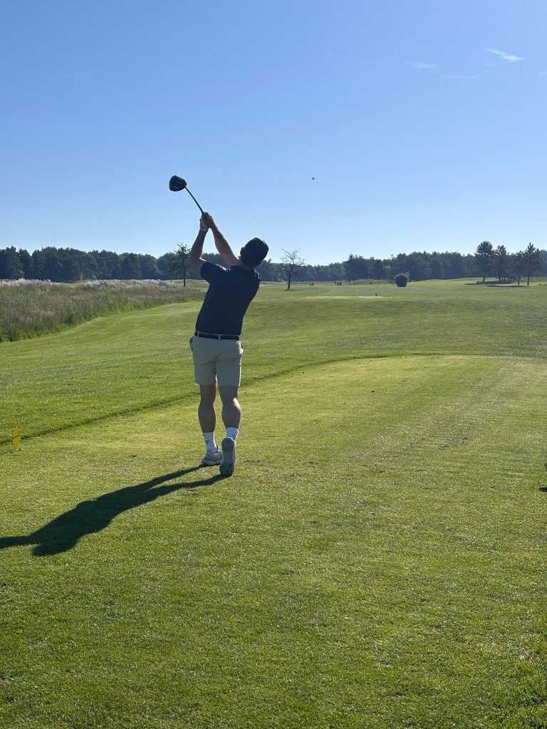 Personne frappant une balle de golf sur un parcours en plein air sous un ciel dégagé.
