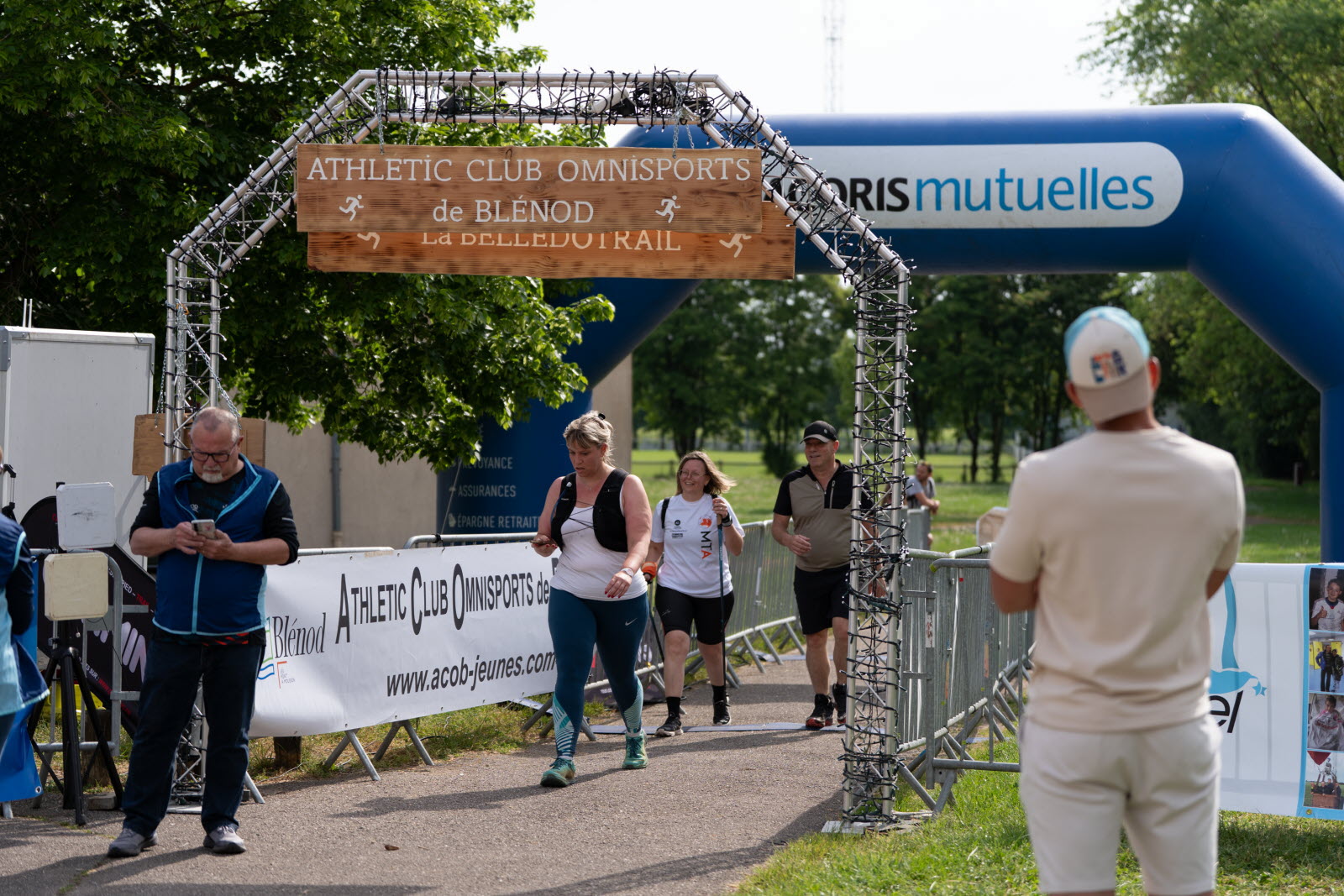 Participants franchissant l’arche d’arrivée de la Bellédotrail à Blénod, avec signalétique ACORIS Mutuelles en arrière-plan.