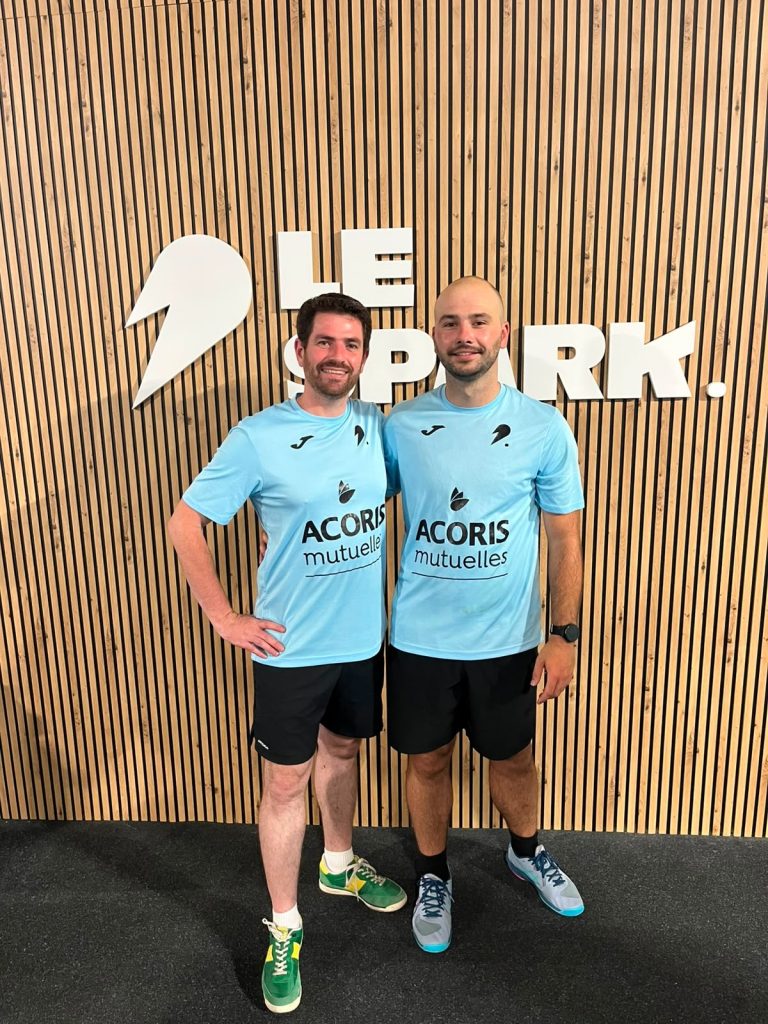 Deux personnes en tenue de sport « ACORIS mutuelles » posent côte à côte devant un mur en bois avec l’inscription « LE SPARK ».