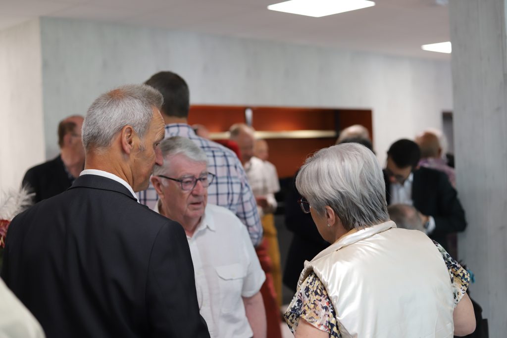 Participants échangent en petits groupes lors d’un moment convivial, debout dans une salle intérieure, avec plusieurs personnes discutant à proximité.