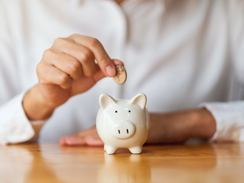 Économies sur la mutuelle santé : main plaçant une pièce dans une tirelire, symbole de la maîtrise du budget, du pouvoir d'achat et du choix d'une complémentaire santé adaptée à ses besoins.