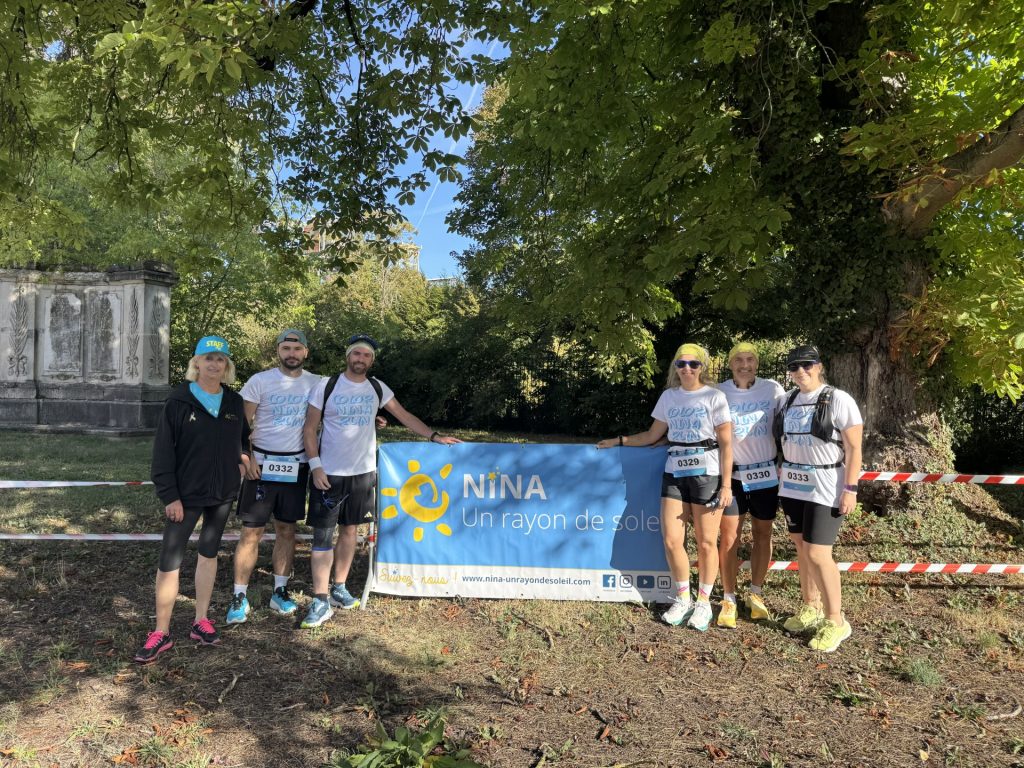 Groupe de six participants et bénévoles réunis dans un parc ombragé autour d’une bannière bleue de l’association Nina, Un rayon de soleil. Les participants portent les t-shirts de la Color Run et posent avant le départ dans un environnement arboré.